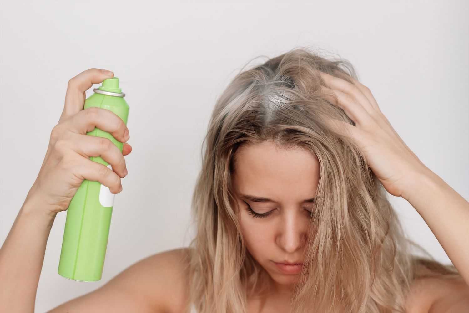 Woman applying dry shampoo to her roots with a green spray can.