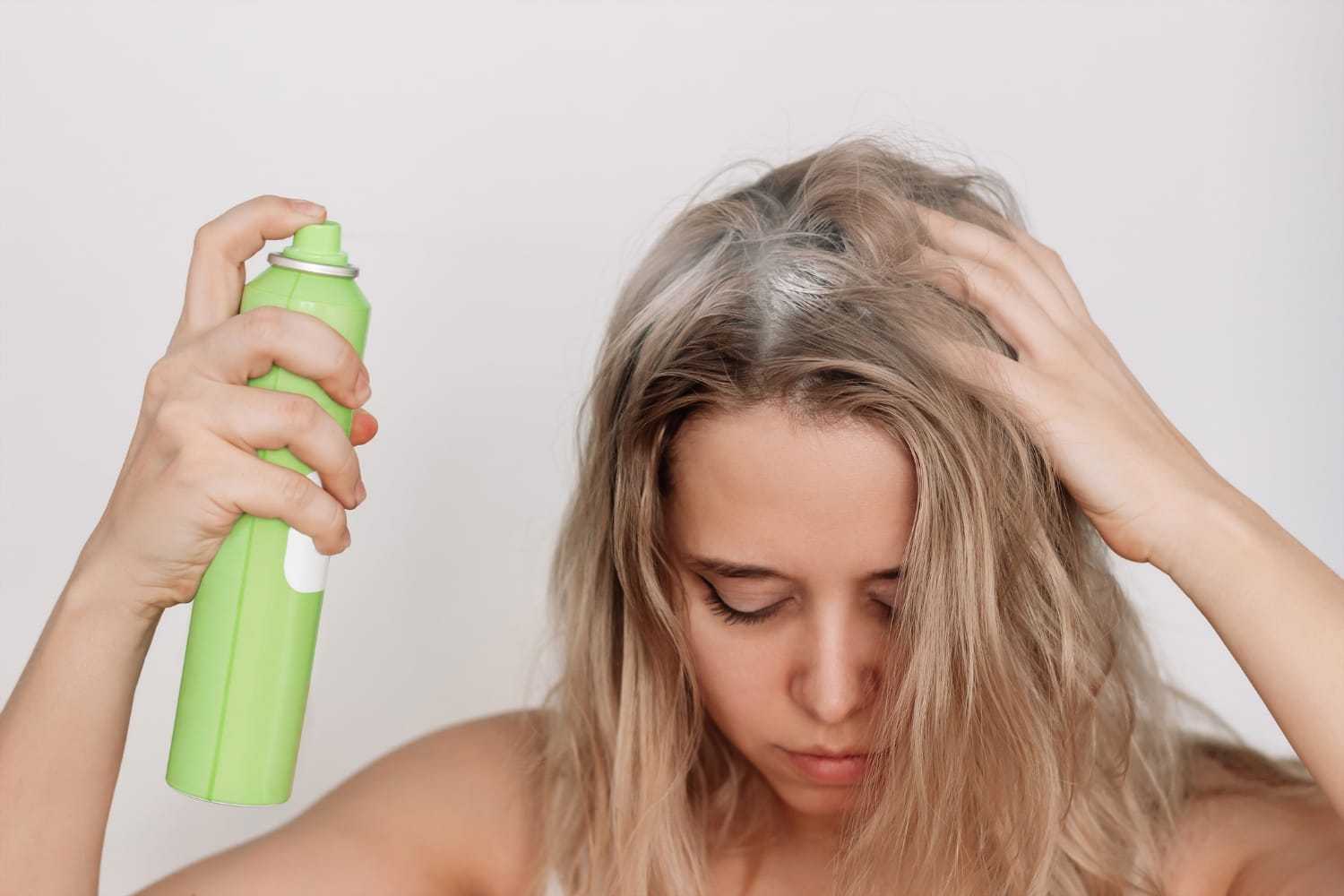 Woman applying dry shampoo to her roots with a green spray can.