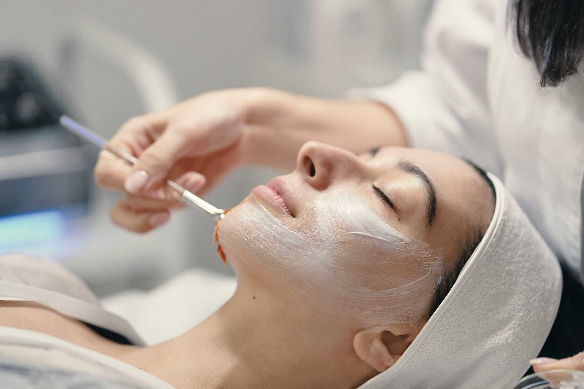 Facial treatment: person with headband receiving mask application, relaxed eyes closed.